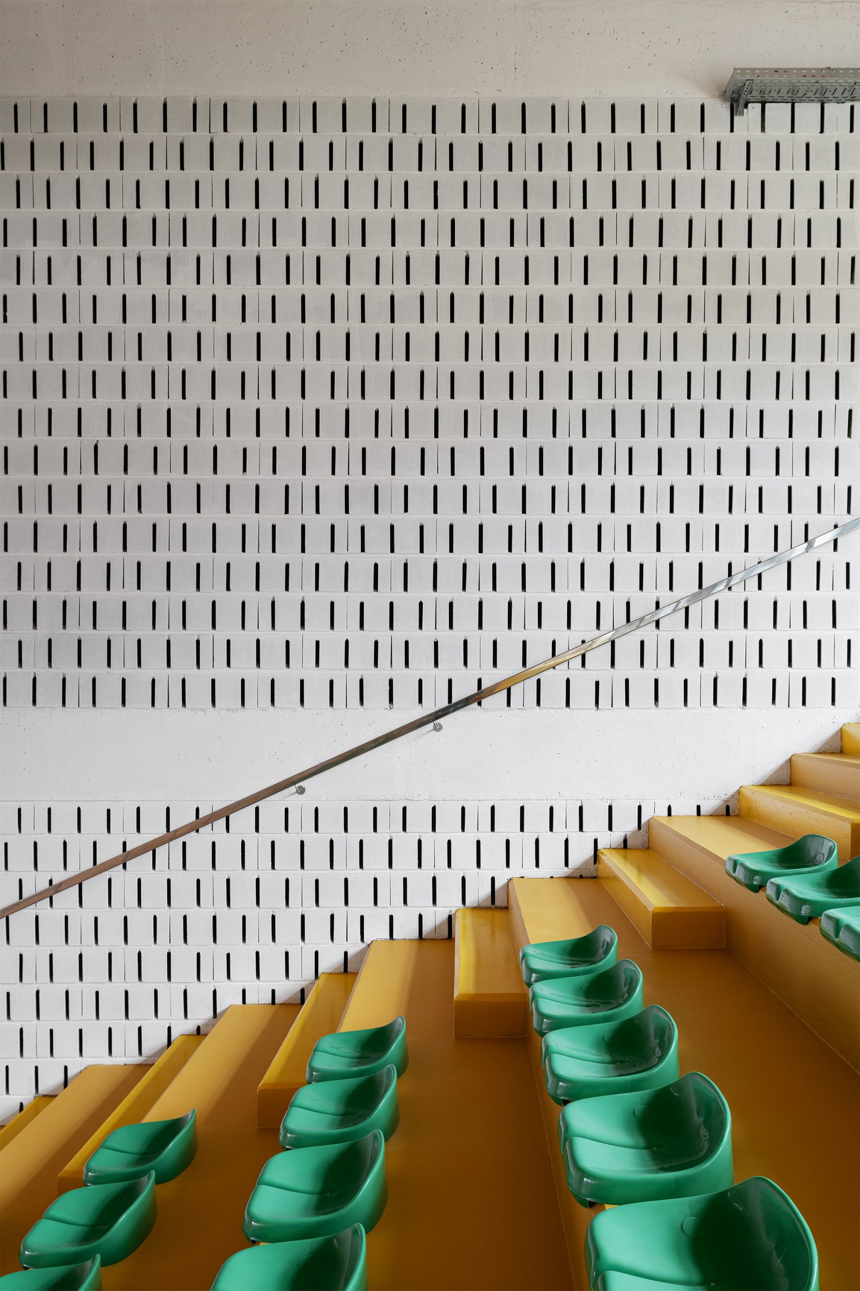 Bancadas amarelas com cadeiras verdes e parede ventilada em bloco branco