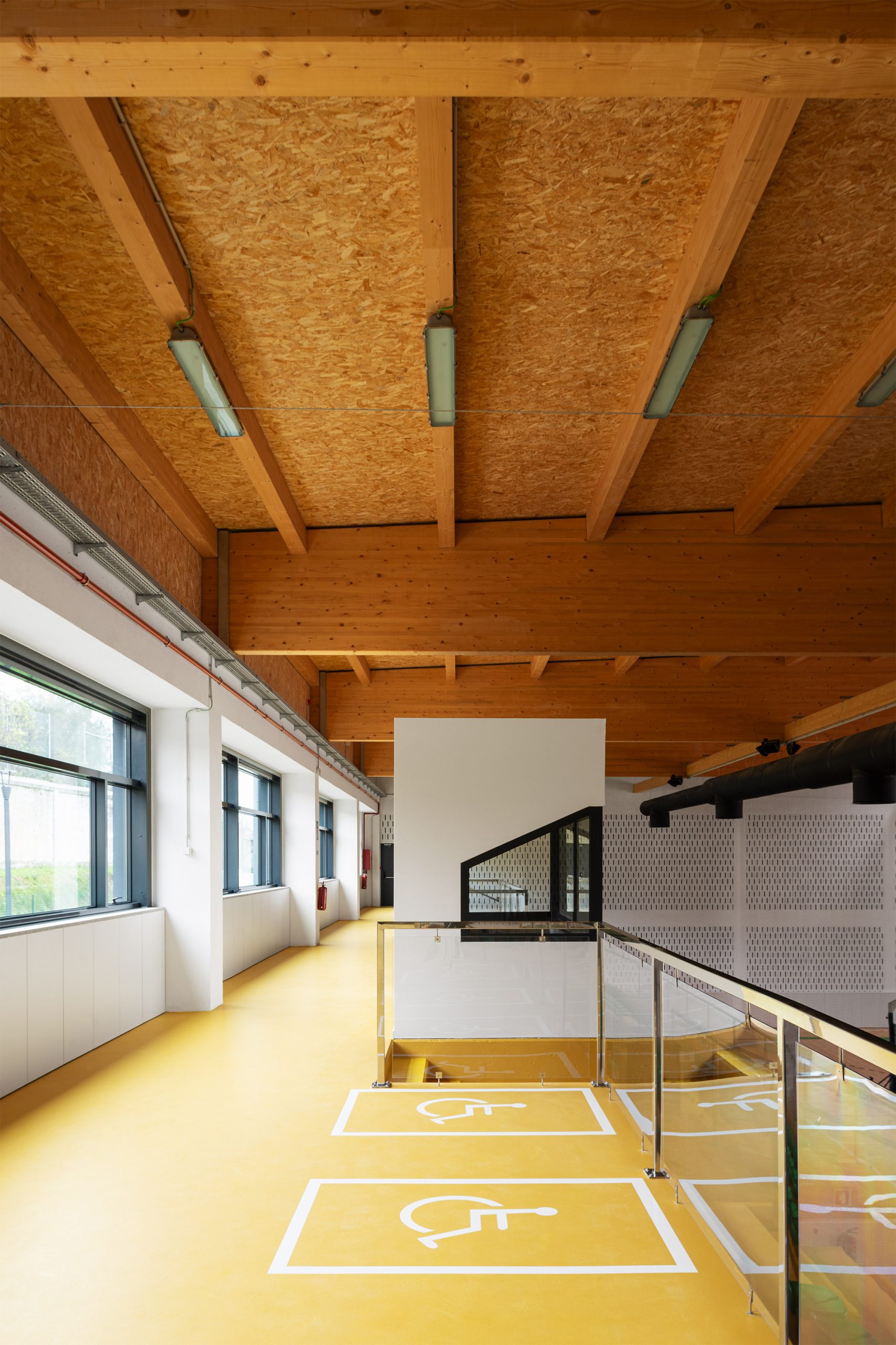 Corredor com piso amarelo e sinalética de acessibilidade junto a guardas envidraçadas