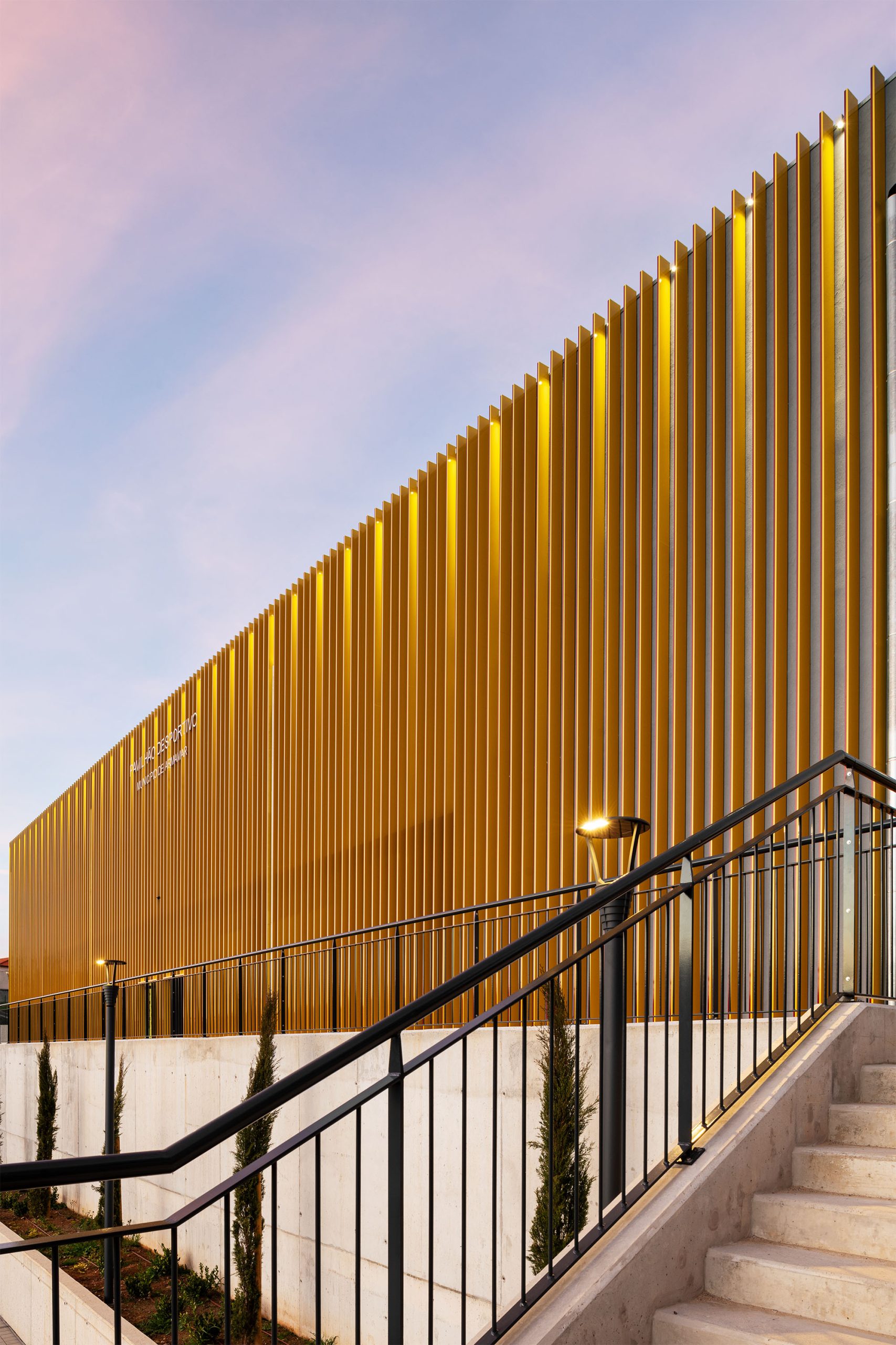 Fachada dourada metálica ao pôr do sol com escadaria frontal em betão