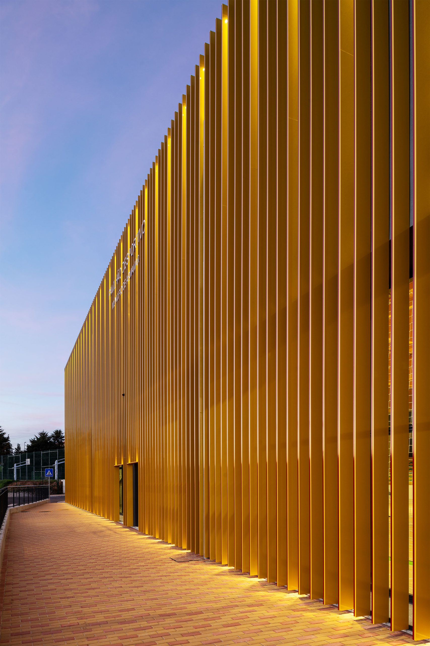 Fachada dourada metálica ao pôr do sol com escadaria frontal em betão