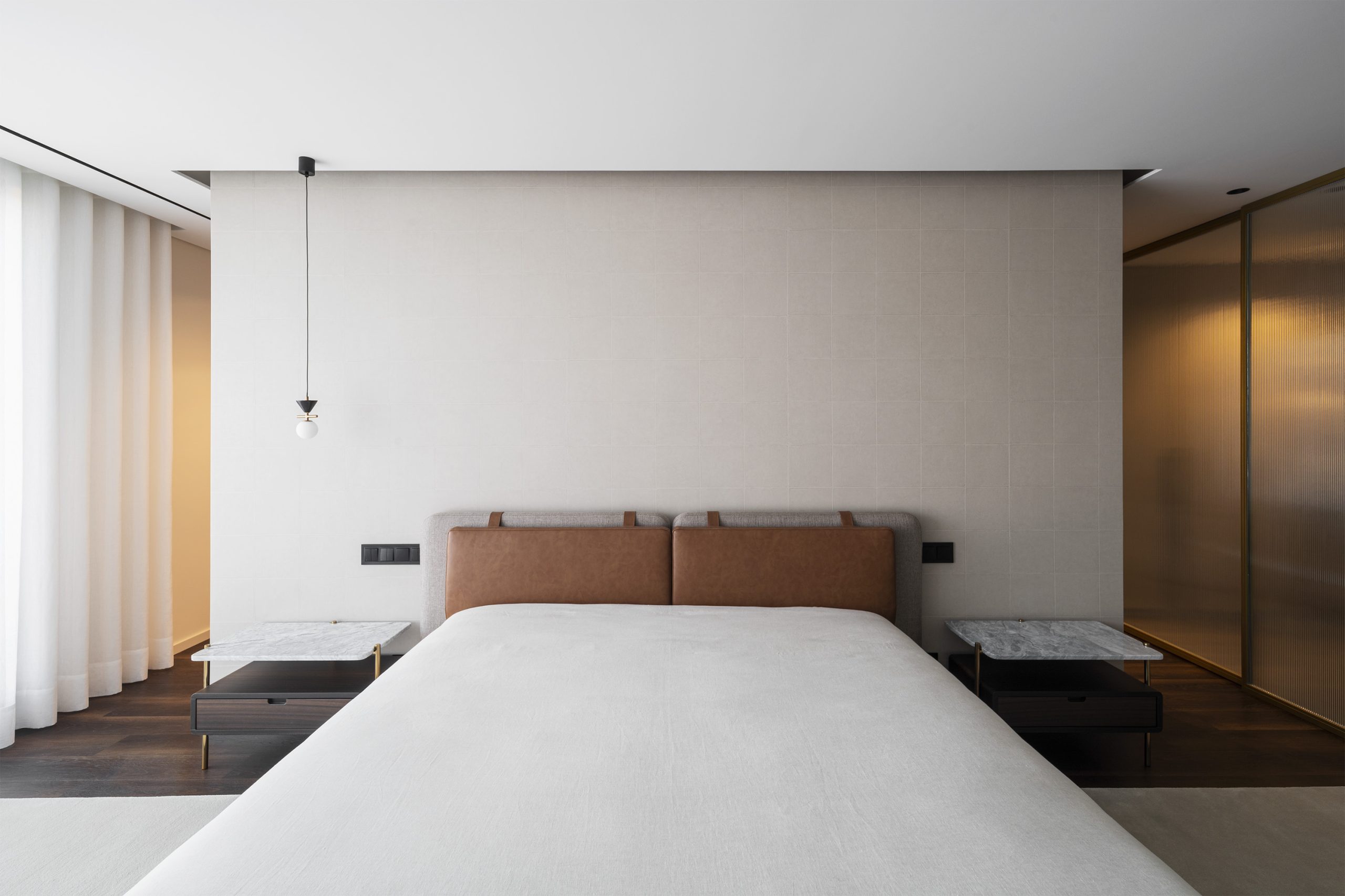 Quarto com cabeceira em pele e pendente minimalista junto a cortina translúcida