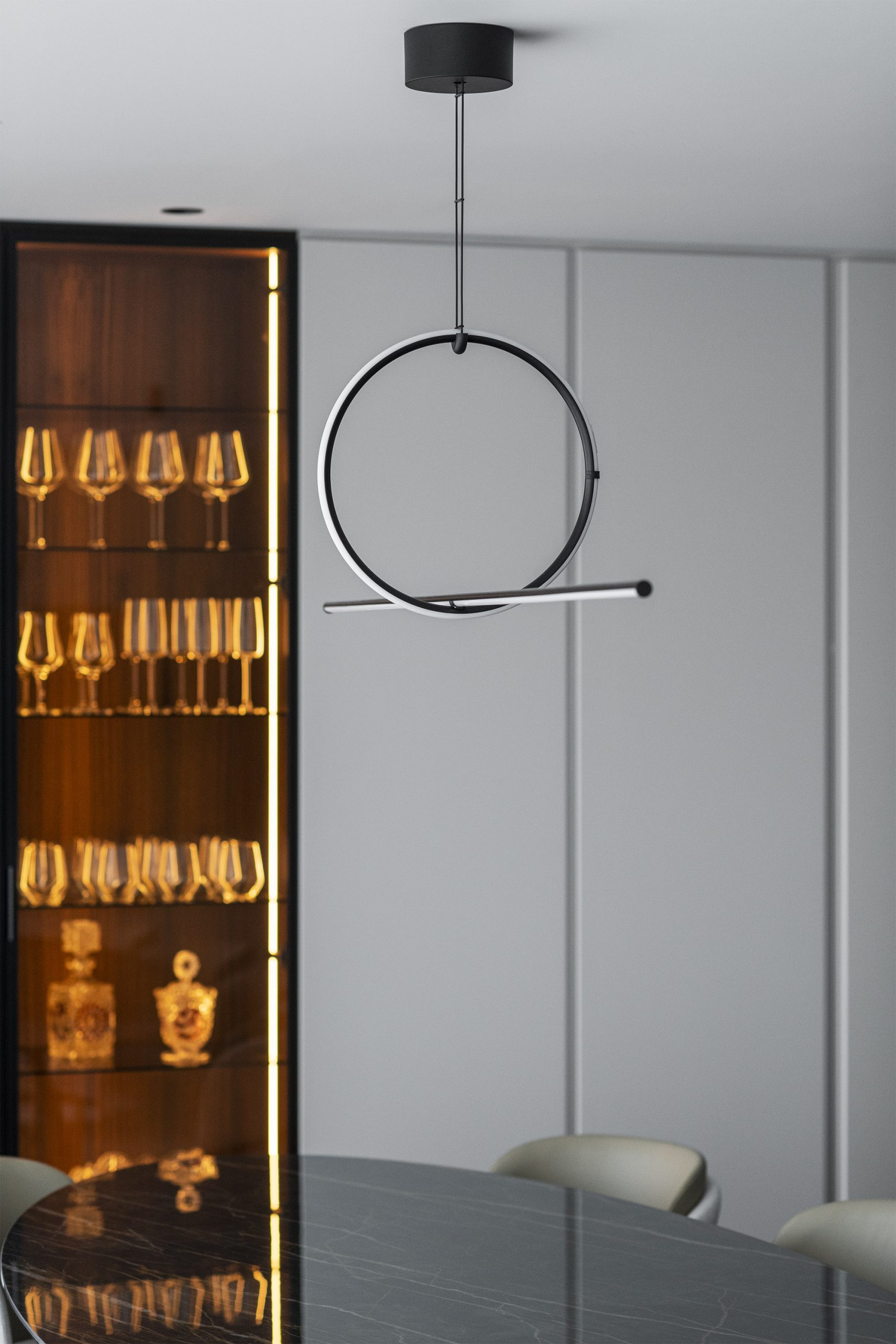 Luminária circular suspensa sobre mesa escura com armário iluminado ao fundo